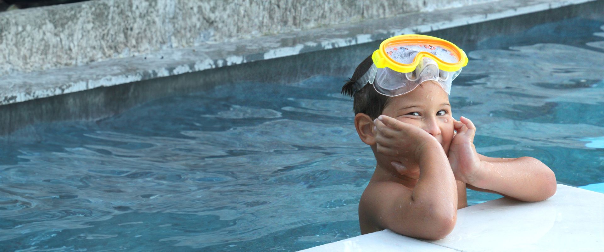 Ein Junge steht am Beckenrand in einem Pool und trägt eine Taucherbrille